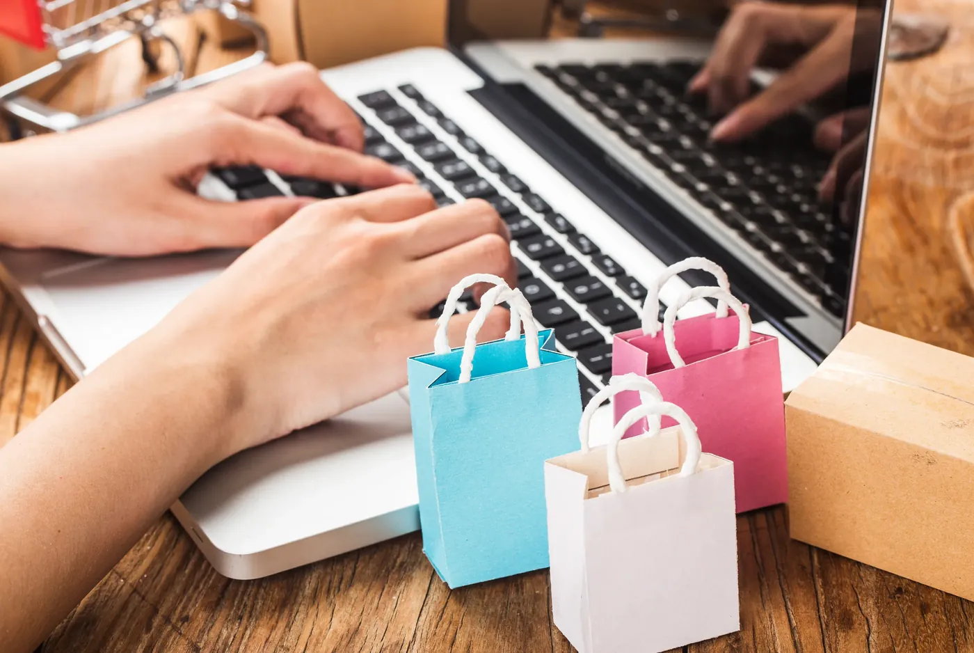 Hands typing on a laptop beside small paper shopping bags, illustrating everyday online buying decisions